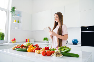 Portrait of attractive cheerful long-haired girl cooking useful salad farm product writing plan list at home light white kitchen indoors