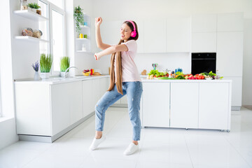 Full length body size view of attractive cheerful long-haired girl dancing having fun in light white home kitchen indoors