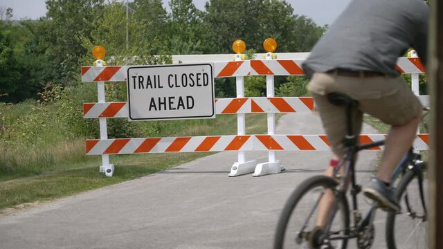 A bicyclist rides past a closed trail sign and takes a detour.  	