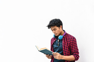 Asian hipster young man reading a book against a white wall - Asian student holding in hands a book...