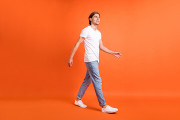 Full size photo of young happy dreamy man walk look empty space travel weekend isolated on orange...