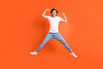 Full body photo of happy cheerful crazy man jump up winner celebrate isolated on orange color background