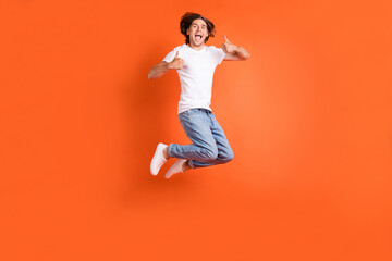 Full length photo of young cheerful positive man jump up show thumbs up smile isolated on orange color background