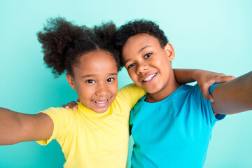Self-portrait of attractive cheerful schoolkids hugging best fellow isolated over bright teal...