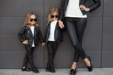 Two sisters with mother in same outfits: white t-shirts, leather black jackets and leggings,...