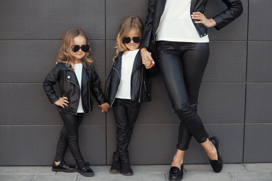 Two sisters with mother in same outfits: white t-shirts, leather black jackets and leggings, sunglasses hearts. Family look concept.