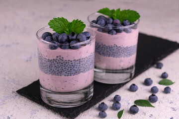 Two glasses with chia pudding with blueberries on a black slate board.