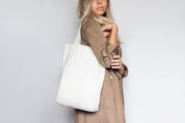 Cropped shot of a young slim woman in a brown coat with an eco linen bag with copy space for text...