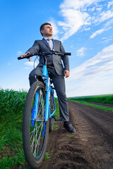 Businessman with a bicycle posing in a green grass field - business concept for freedom, vacation or freelance. Beautiful spring nature.