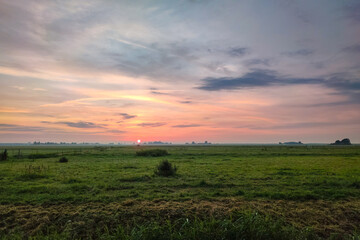 The sun sets over the wide open Dutch landscape, casting beautiful colors over the green meadows