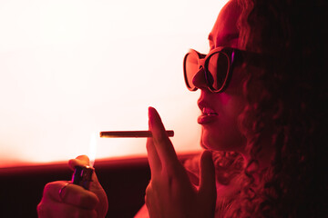 Chica encendiendo un cigarro en el coche con gafas de sol y luz roja