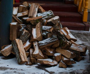 A large pile of chopped firewood under a thin layer of fresh snow near the porch