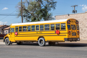 Naklejka na ściany i meble Yellow USA full-sized Schoolbus parked on street of small town