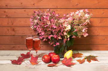Autumnal pink hydrangea flowers, rose champagne and fresh fruits on aged wooden table.