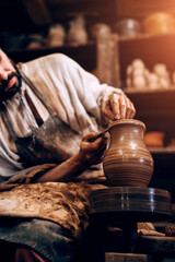 The potter professionally forms the shape of a bowl on a potter wheel from a damp piece of clay - obrazy, fototapety, plakaty