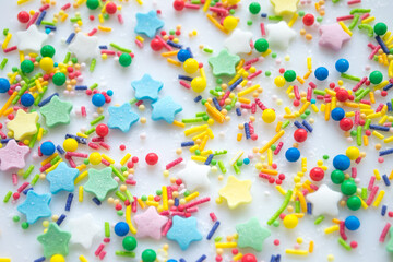 Multi-color festive background of a scattering of sugar candy sprinkles for cupcakes and other pastries in form of stars, sticks and balls. Pastel colors of red, pink and green, blue and yellow