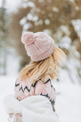 Close up portrait of an beautiful girl in a woolen sweater enjoying winter moments. Outdoors photo of a short-haired lady in a pink hat having fun on a snowy morning on a blurred nature background.