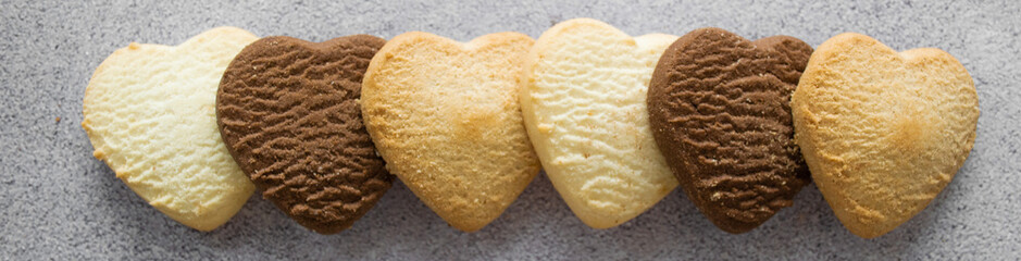 Banner with multicolored cookies in the shape of a heart: vanilla, lemon, chocolate. Gray background