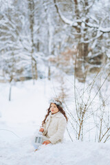 Little charming little girl in a Christmas wreath sitting in the snow with a lantern in her hands. .Winter day outdoors