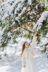 Little girl shaking the branch of pine tree covered by snow.
