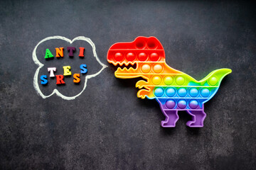 Toy pop it dinosaur rainbow colors on a black background with multicolored letters and the inscription-Anti-stress in a speech bubble