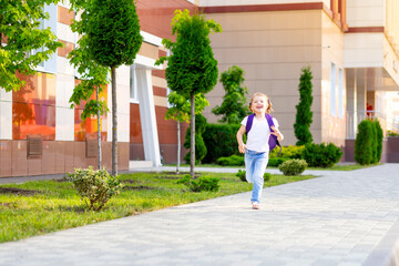 Fototapeta na wymiar a child schoolgirl with a backpack jumps with happiness and runs to school on the first day of autumn, the concept is back to school