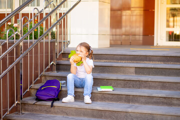 a child schoolgirl eats lunch or a burger snack before school, a concept of back to school or...
