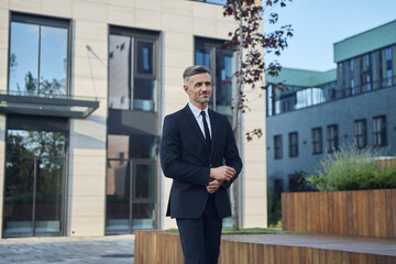Confident mature businessman walking near office building outdoors