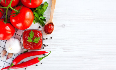 Ripe tomatoes and red ketchup on a white wooden background. Close-up. Top view. Place for text.
