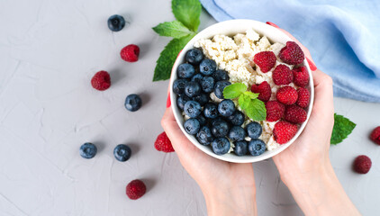 Female hands hold a bowl with cottage cheese and fresh berries. Healthy breakfast in the morning. ?lose-up. Top view. Copy space.