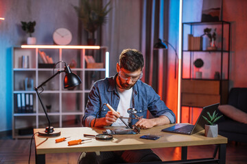 Handsome 35-aged bearded man in protective glasses sitting at table and soldering video card from...