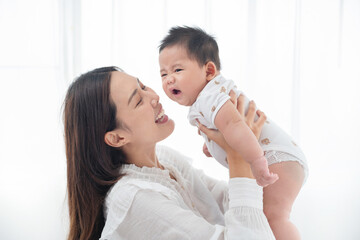 Happy family. Laughing mother lifting her adorable newborn baby son in air, copy space. asian mother lifting and playing with newborn baby, Health care family love together. Asian girl lifestyle.