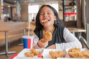 Close up portrait of a satisfied pretty  little asian girl eating fried chicken and french fries In...