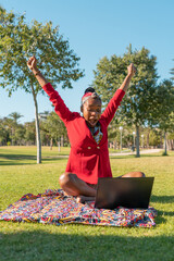 Chica emocionada con brazos arriba con expresión de felicidad, sentada en el parque con el...