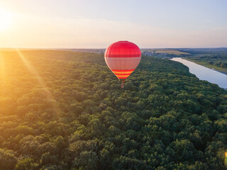 Hot air red balloon flies over the river and forest in the evening