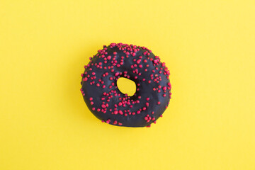 Top view of donut with black glaze on the yellow background. Close-up.
