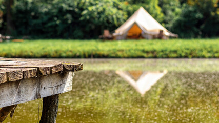 Naklejka premium Wooden pier for rest near a lake with tent on the background at glamping