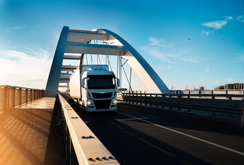 Cargo truck with trailer crossing modern bridge at sunset 