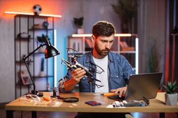 Fototapeta na wymiar Handsome bearded man using wireless laptop for searching for solution of fixing modern quadcopter. Concept of people, technology and repairing.