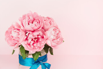 Gentle pink peonies in a glass vase with a blue satin ribbon. Elegant pink floral background. Copy Space. Greeting card. Minimalistic floral background