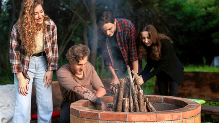 A group of happy young friends trying to make a campfire at glamping