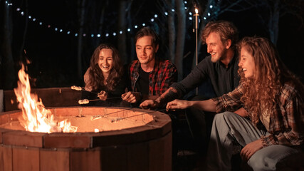 A group of happy young friends near a campfire at glamping, night