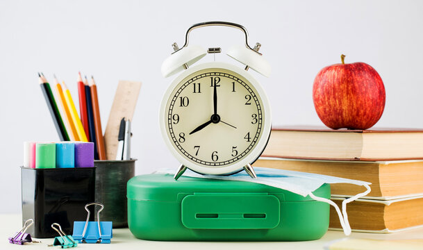 Back to school. A composition of school supplies, an alarm clock and a protective mask.