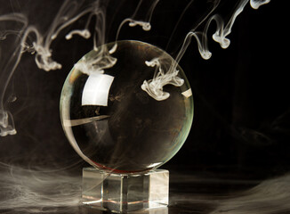 Crystal ball reflecting a black background and falling smoke, selective focus.