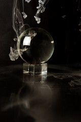 Crystal ball reflecting a black background and falling smoke, selective focus.