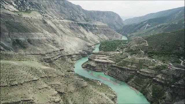 Aerial view of a curving green river flowing among rock slopes. Action. Summer natural landscape with a picturesque stream and mountain range.