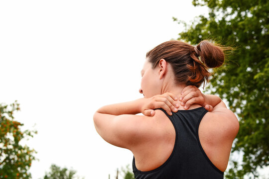 A young woman holds her hands on her neck, doing self-massage, her head is turned to one side, a view from the back, after sports, relaxes her neck, on the way to a healthy and strong body.