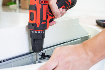 man assembling white table furniture at home using cordless screwdriver