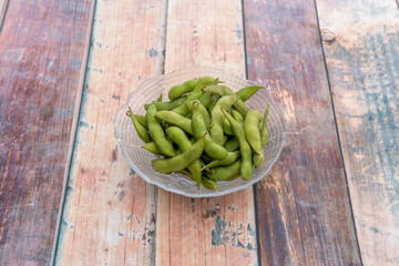 Transparent glass bowl with Asian edamame pods on wooden table