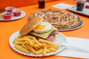 Burger with fried yellow yolk egg with veal with melted cheese, fried bacon and potato garnish served in a pizzeria